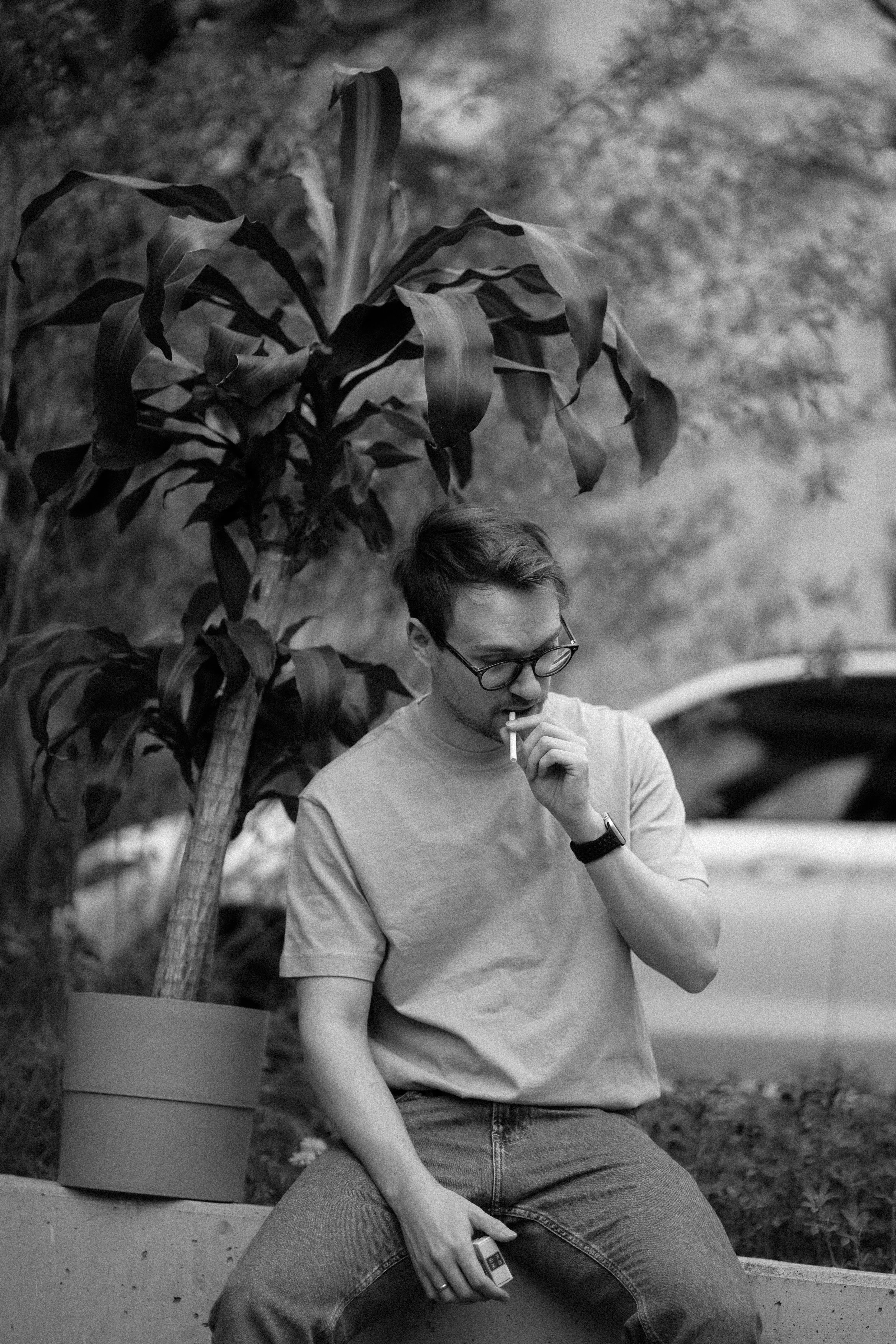 A seated man beside a potted plant in a monochrome photograph